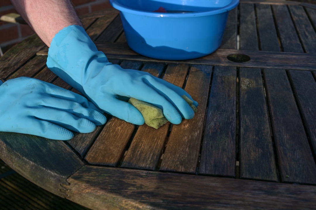 Cleaning wood patio table wearing rubber gloves